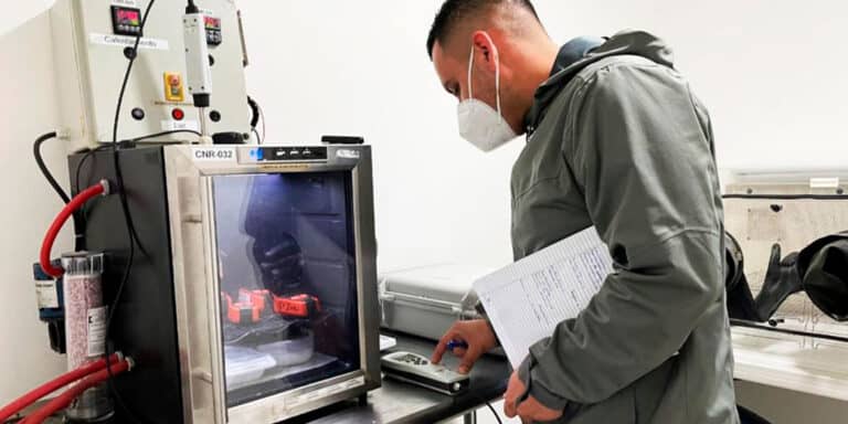 Técnico con mascarilla operando equipo de cámara de prueba CNR-032 con control remoto y hoja de registro en laboratorio