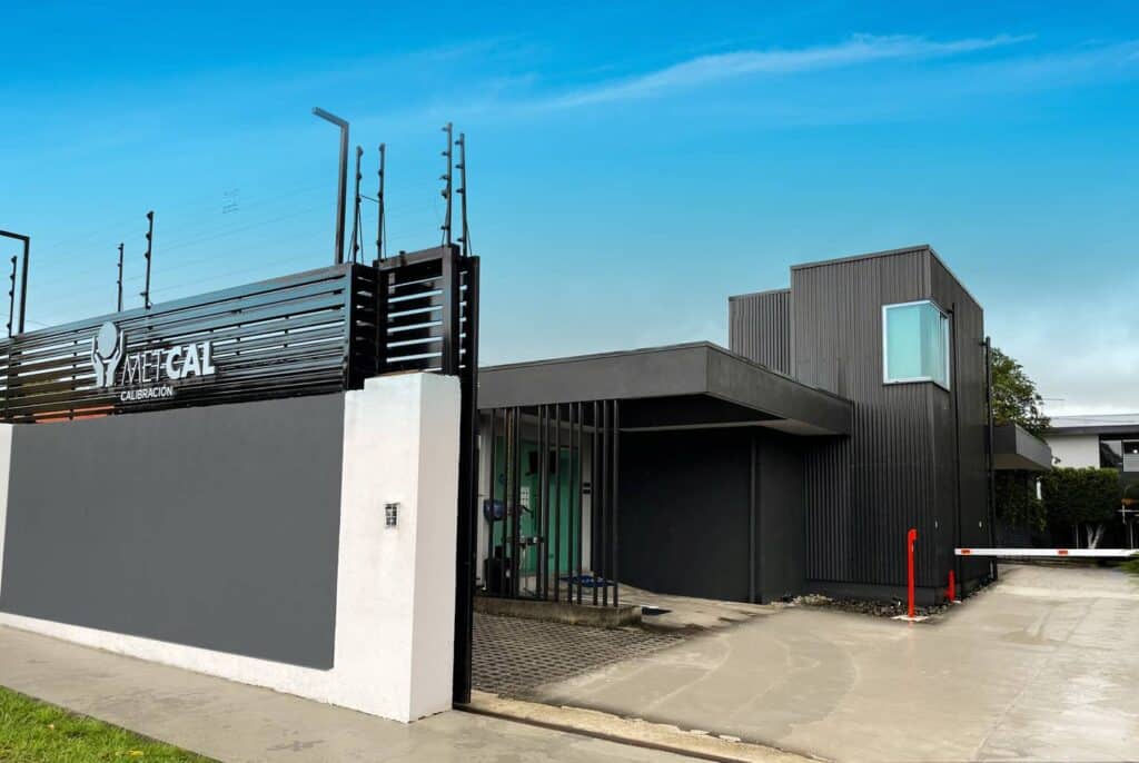 Fachada moderna del centro de calibración Metcal con muro de entrada, edificio de dos plantas en tonos gris y negro, y barrera de acceso