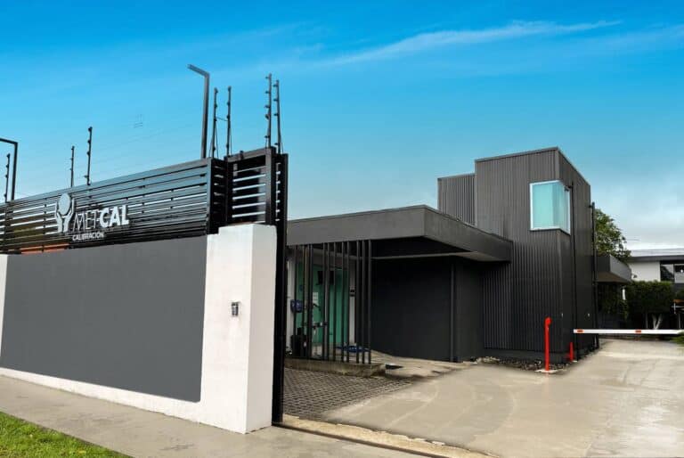 Fachada moderna del centro de calibración Metcal con muro de entrada, edificio de dos plantas en tonos gris y negro, y barrera de acceso