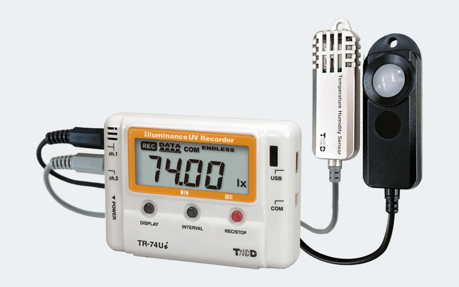 Registrador T&D TR-74Ui de iluminancia, UV, temperatura y humedad con sensores externos, pantalla digital y conexiones USB, diseñado para monitorización ambiental sobre fondo gris claro